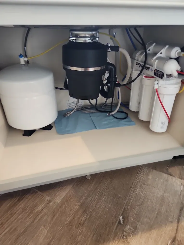 A garbage disposal under a kitchen sink, beside a water filter system
