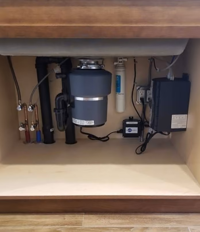 A garbage disposal under a sink, beside a water filter and new shut-off valves