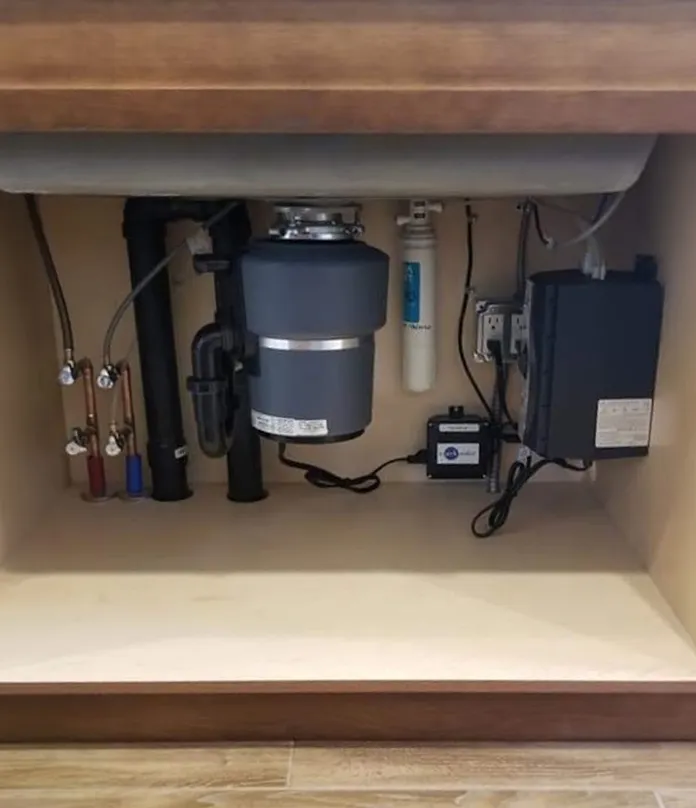 A garbage disposal under a sink, beside a water filter and new shut-off valves.