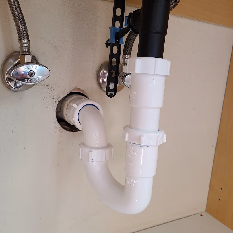 A new white drain trap and shut-off valves under a sink