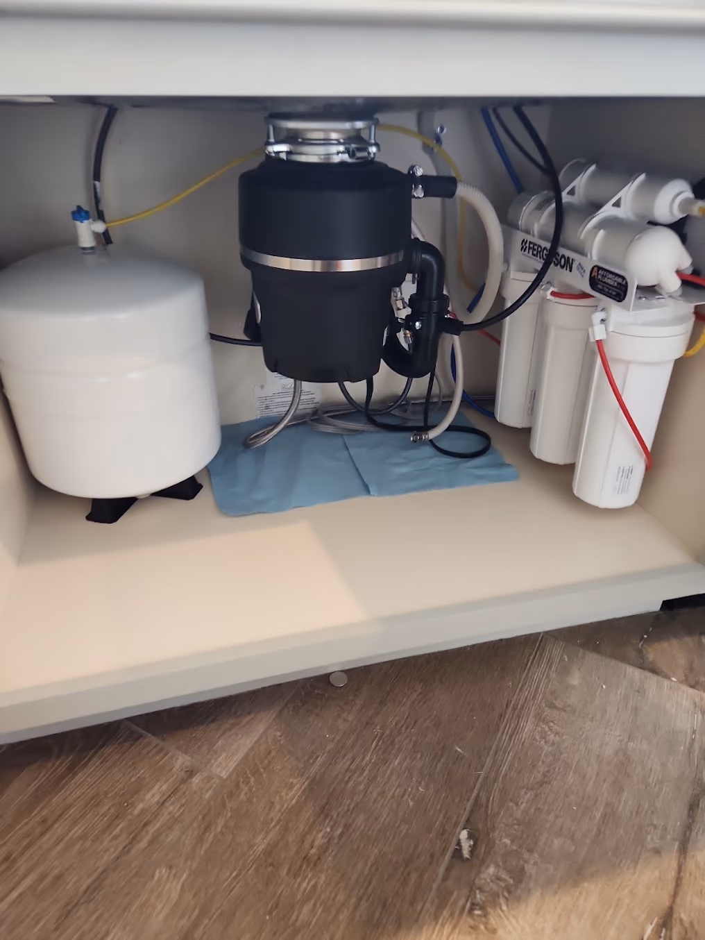 A garbage disposal under a kitchen sink, beside a water filter system