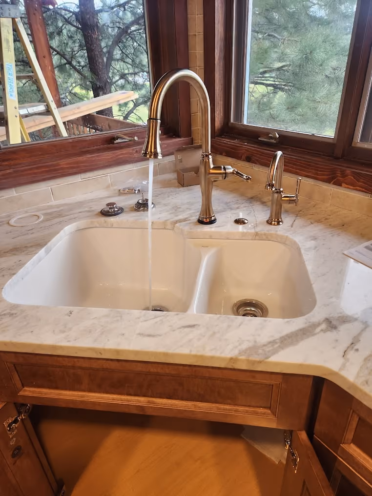A brass kitchen faucet running into a white double sink
