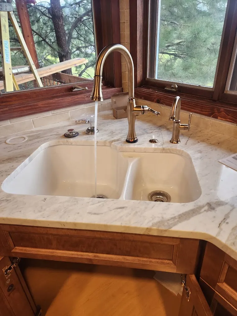 A brass kitchen faucet running into a white double sink.