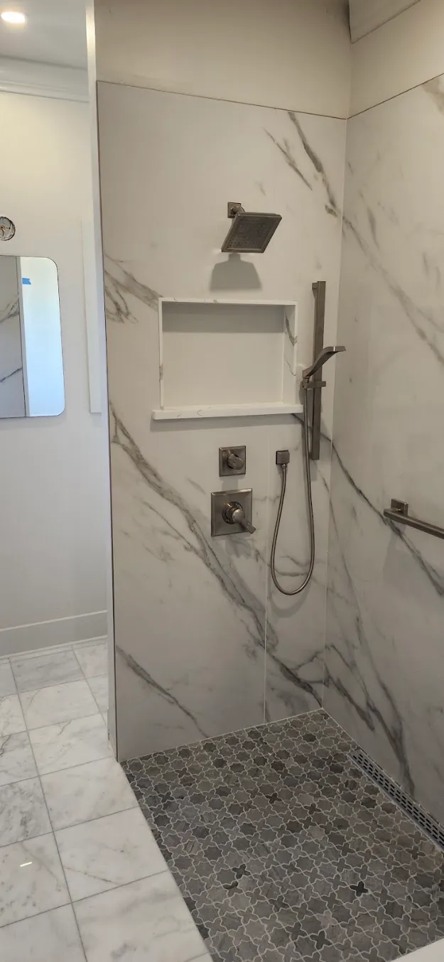 A shower valve and hand shower in a marble shower.