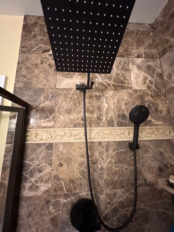 A rain shower head and hand shower in a tiled shower