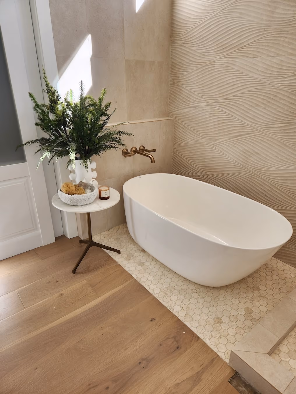 A freestanding soaking tub with a wall-mounted brass faucet