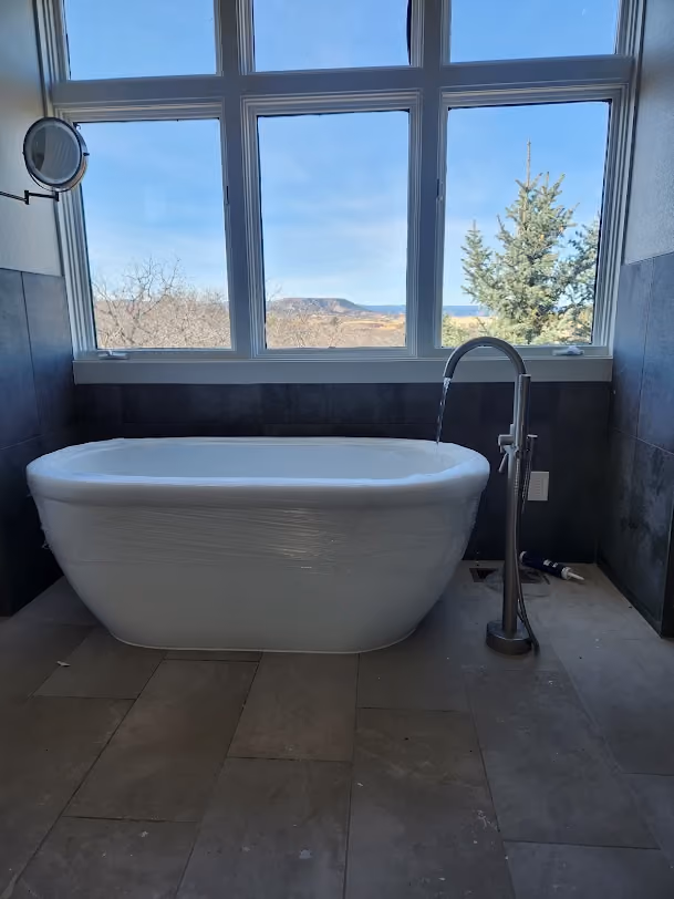 A freestanding tub with a floor-mounted filler beside a window