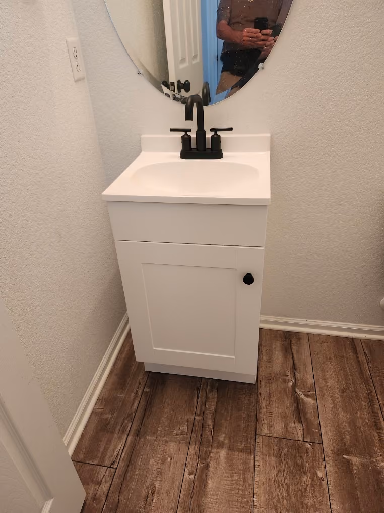A new white vanity with a black faucet in a small bathroom