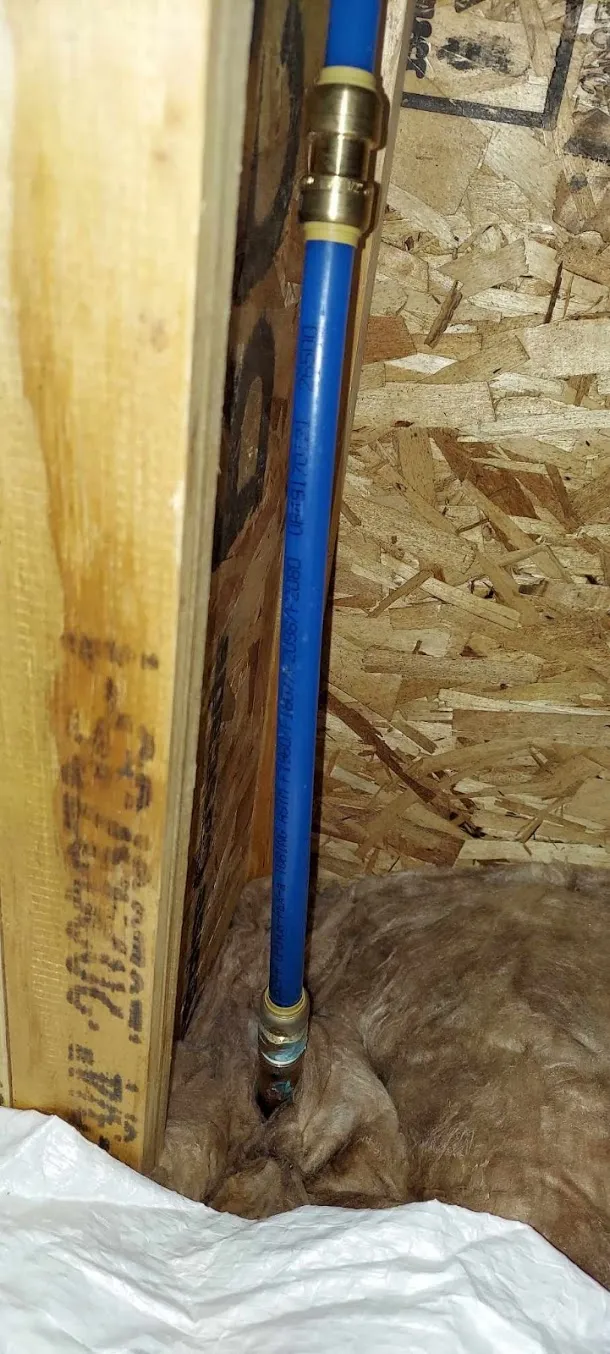 A wall opened up to reach a leak, with water staining on the stud beside the pipe.