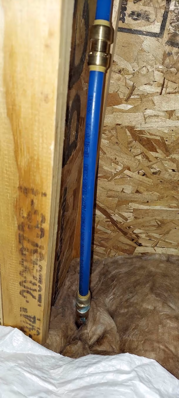 A wall opened up to reach a leak, with water staining on the stud beside the pipe