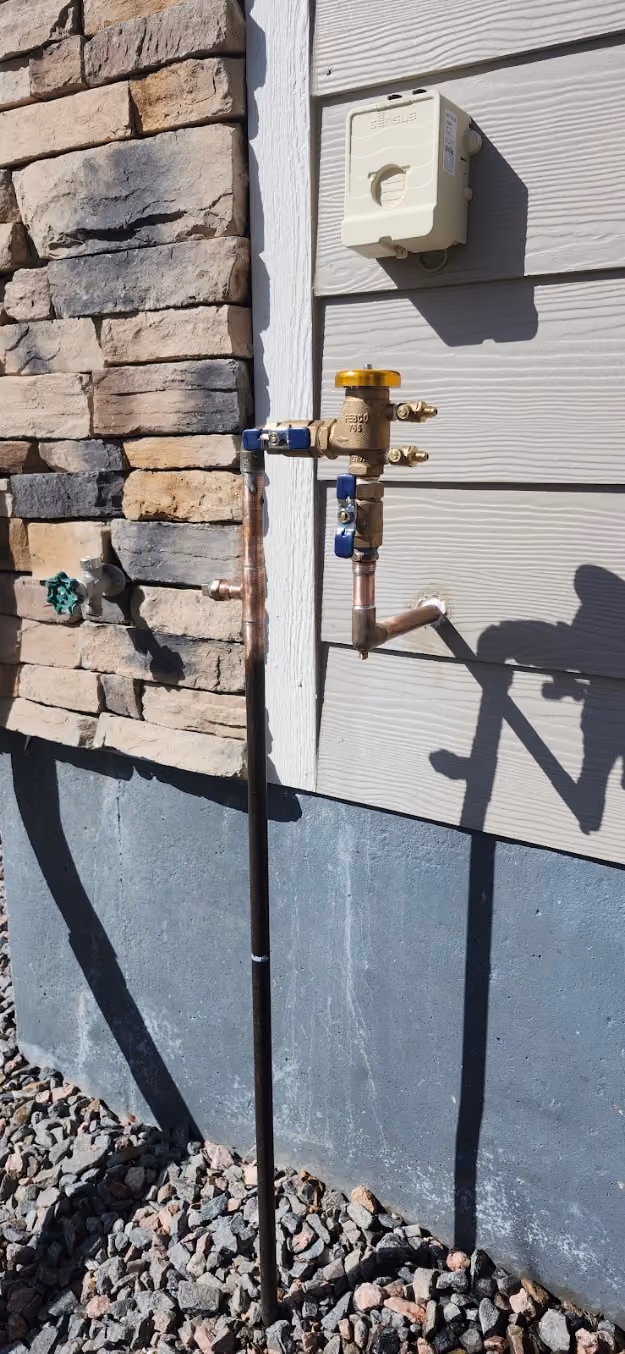 A backflow preventer beside a stone wall