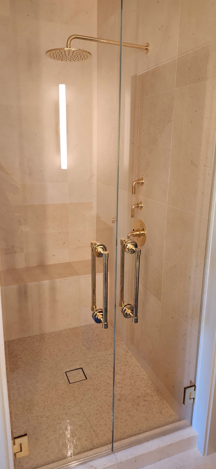 A walk-in shower with a brass shower valve, rain head and glass door