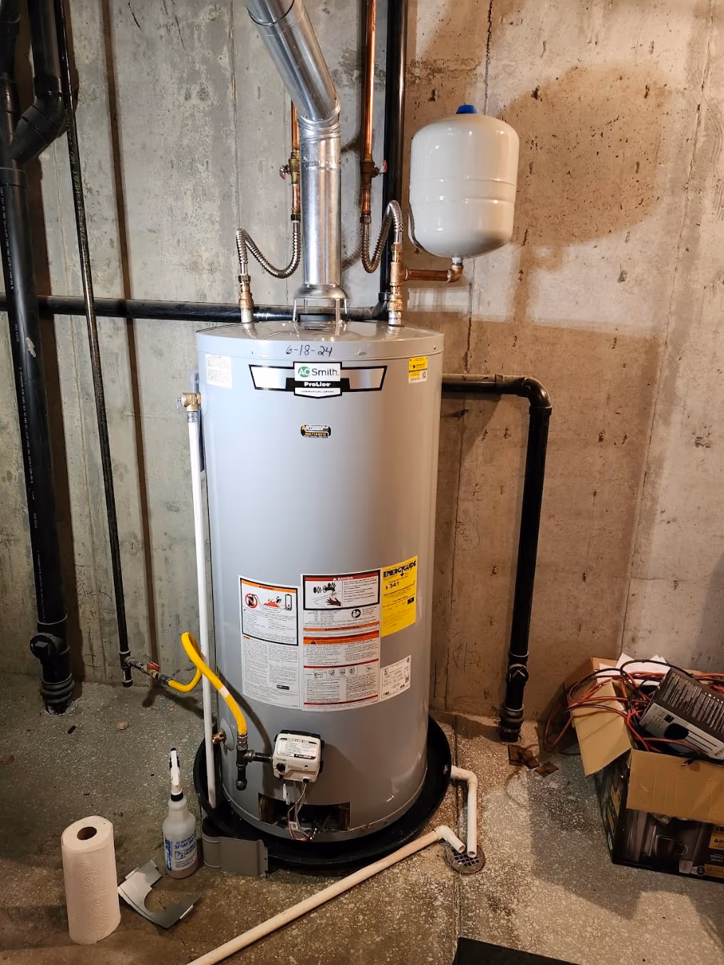 A new water heater in an unfinished basement, with an expansion tank above it