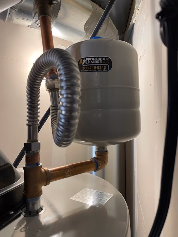 An expansion tank with an Affordable Plumber sticker on a water heater's cold line